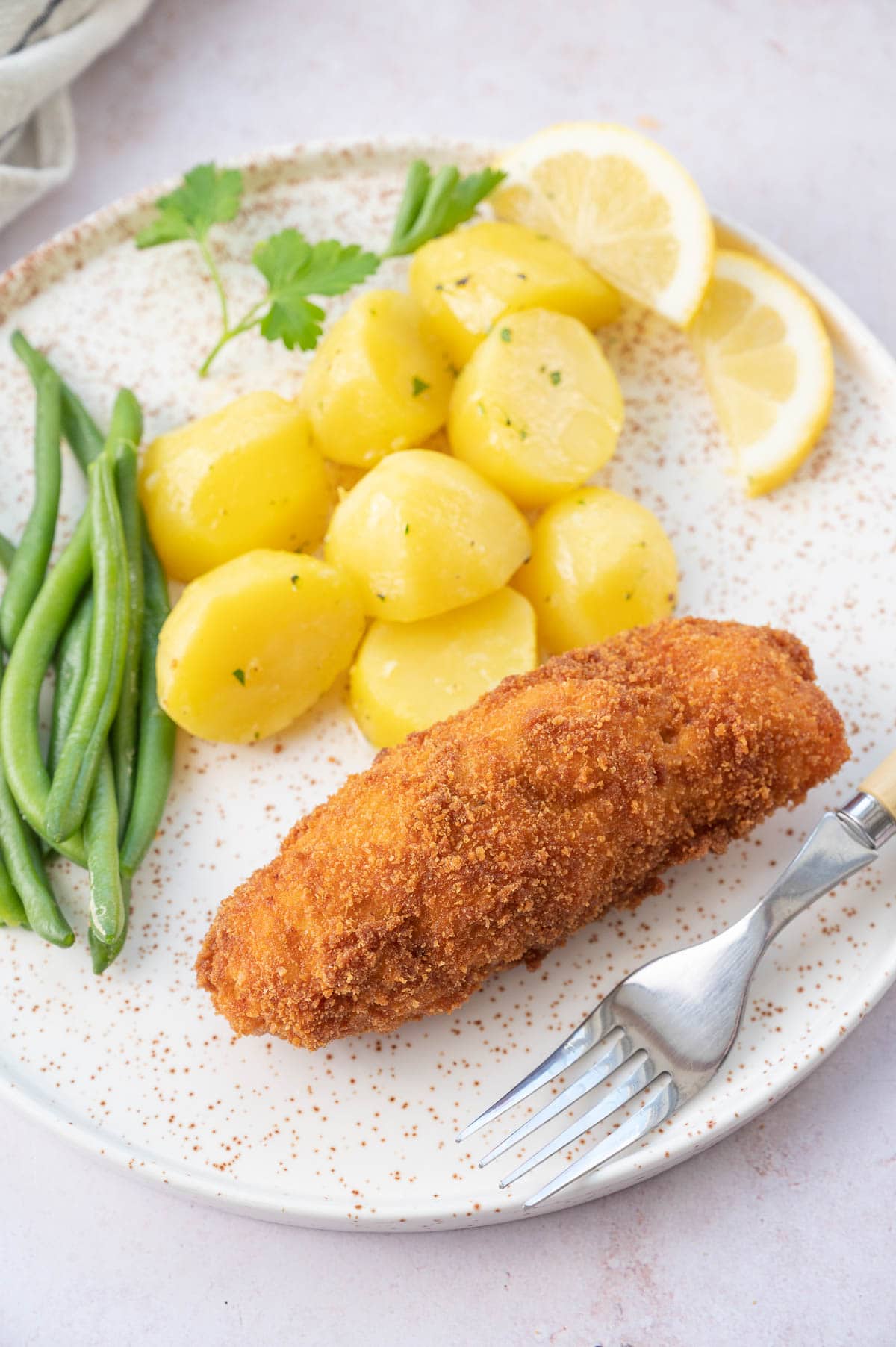 Chicken Kyiv with potatoes and green beans on a white plate.