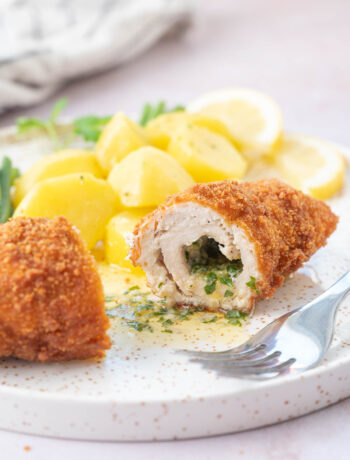 Chicken Kyiv cut in half on a white plate with potatoes.