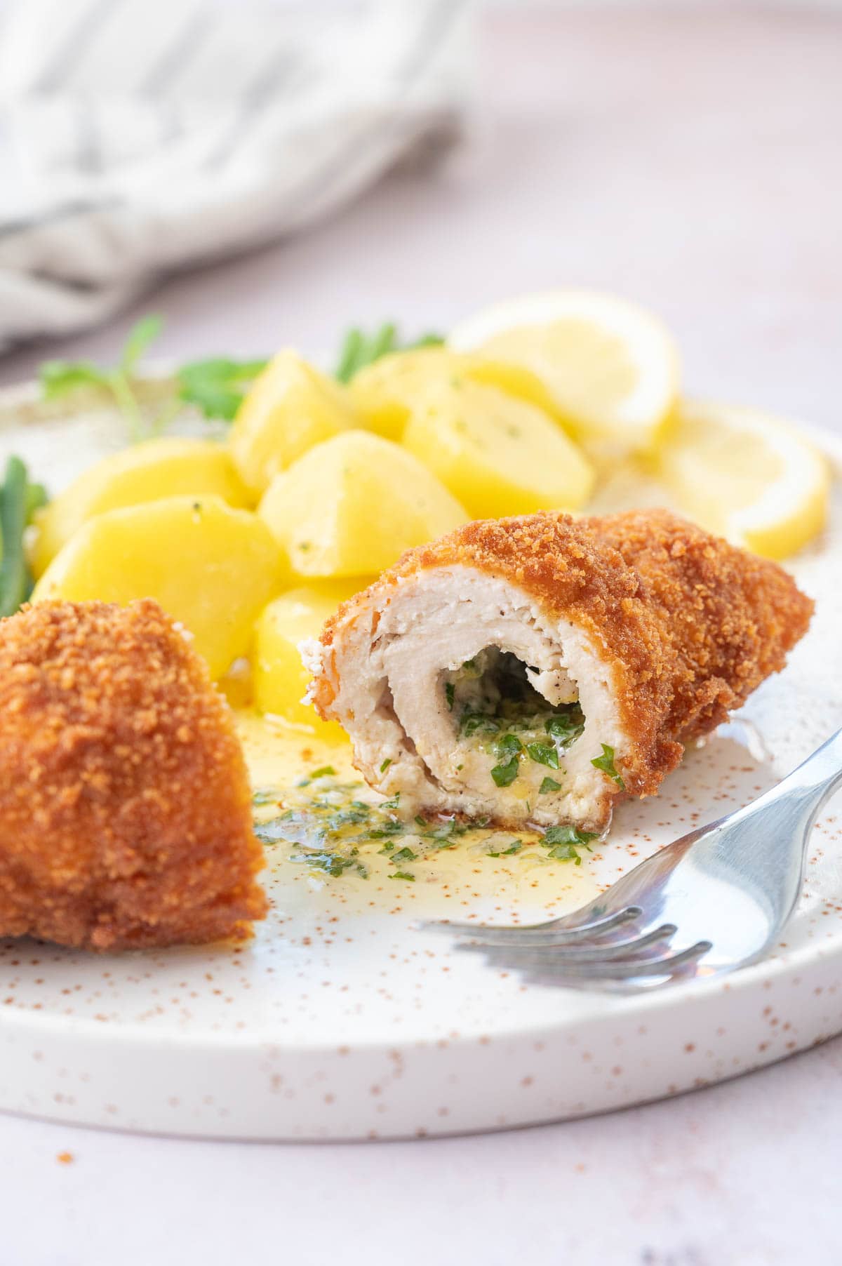 Chicken Kyiv cut in half on a white plate with potatoes.