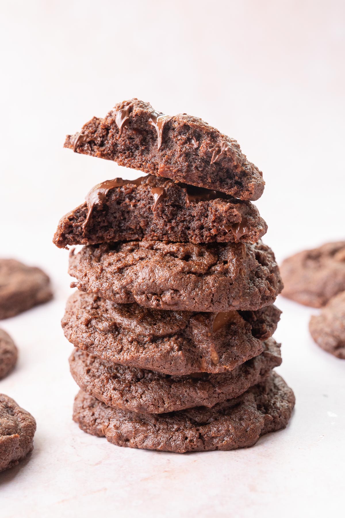 A stack of double chocolate chip cookies. The top cookie is broken in half to show the inside.