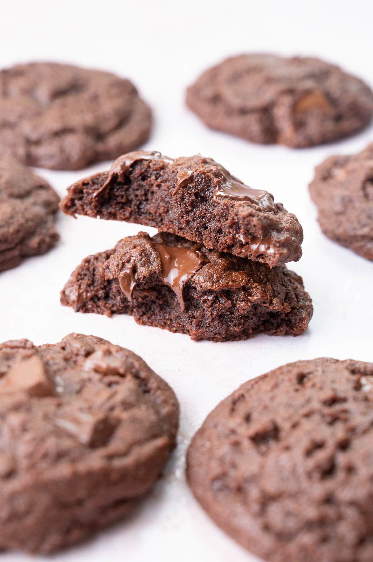 Two halves of double chocolate chip cookies on a light background. More cookies in the background.