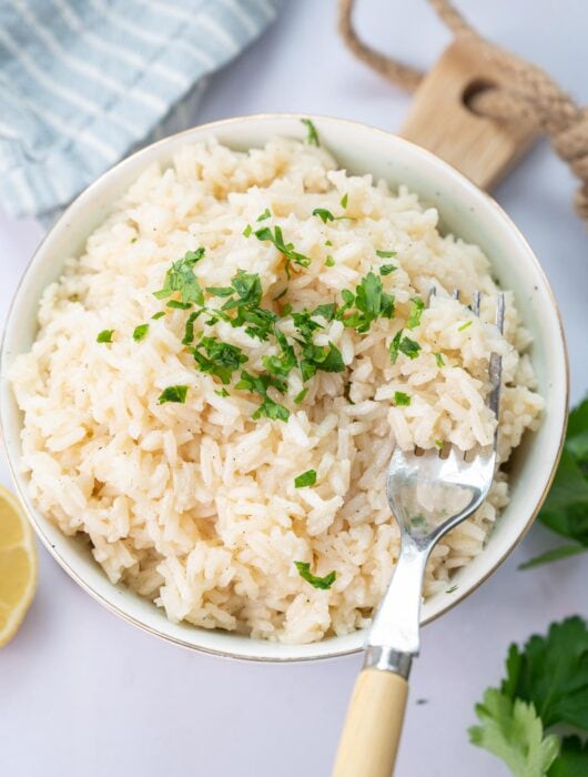Garlic butter rice in a white bowl topped with chopped parsley with a fork on the side.