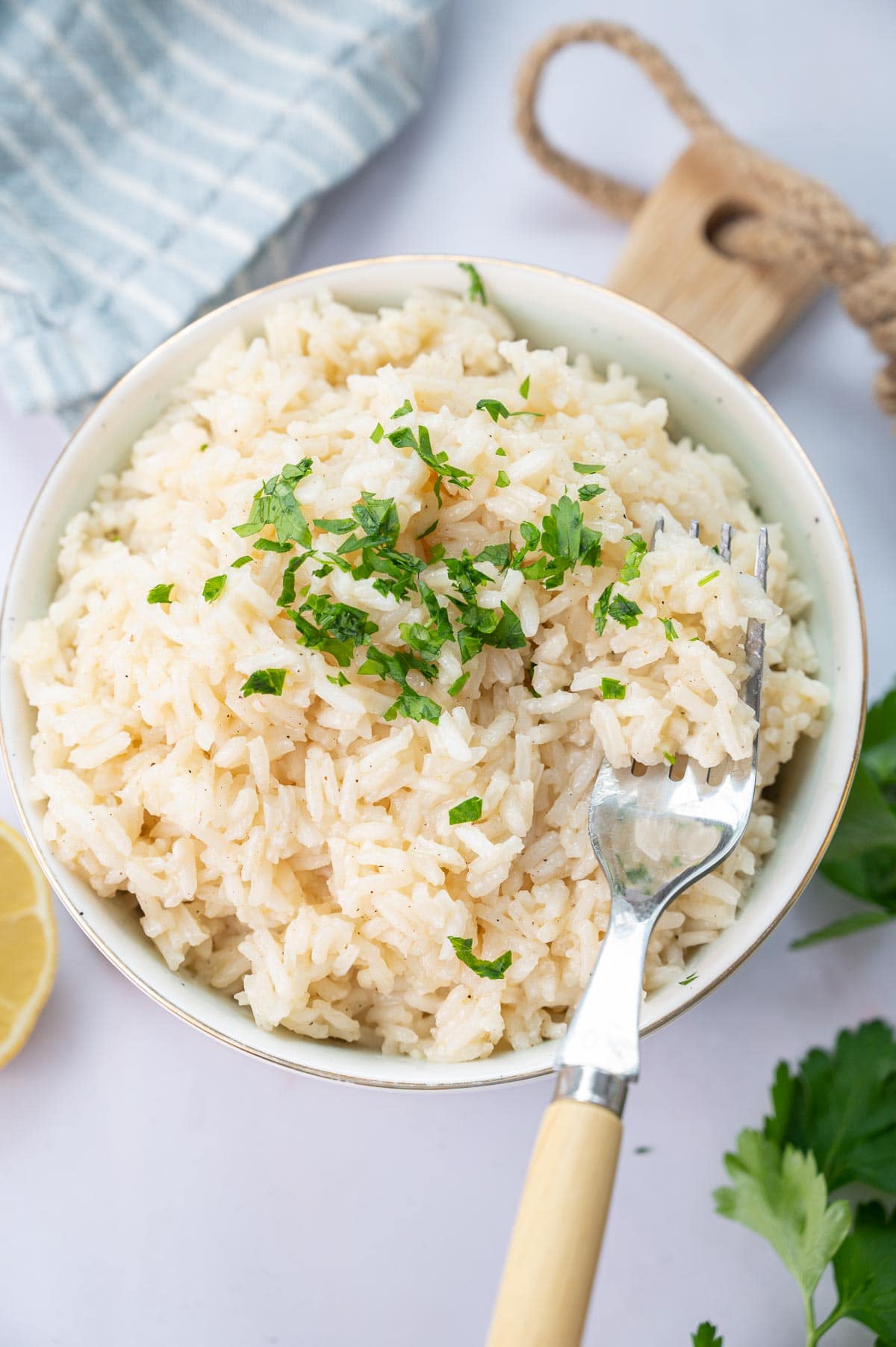 Garlic butter rice in a white bowl topped with chopped parsley with a fork on the side.