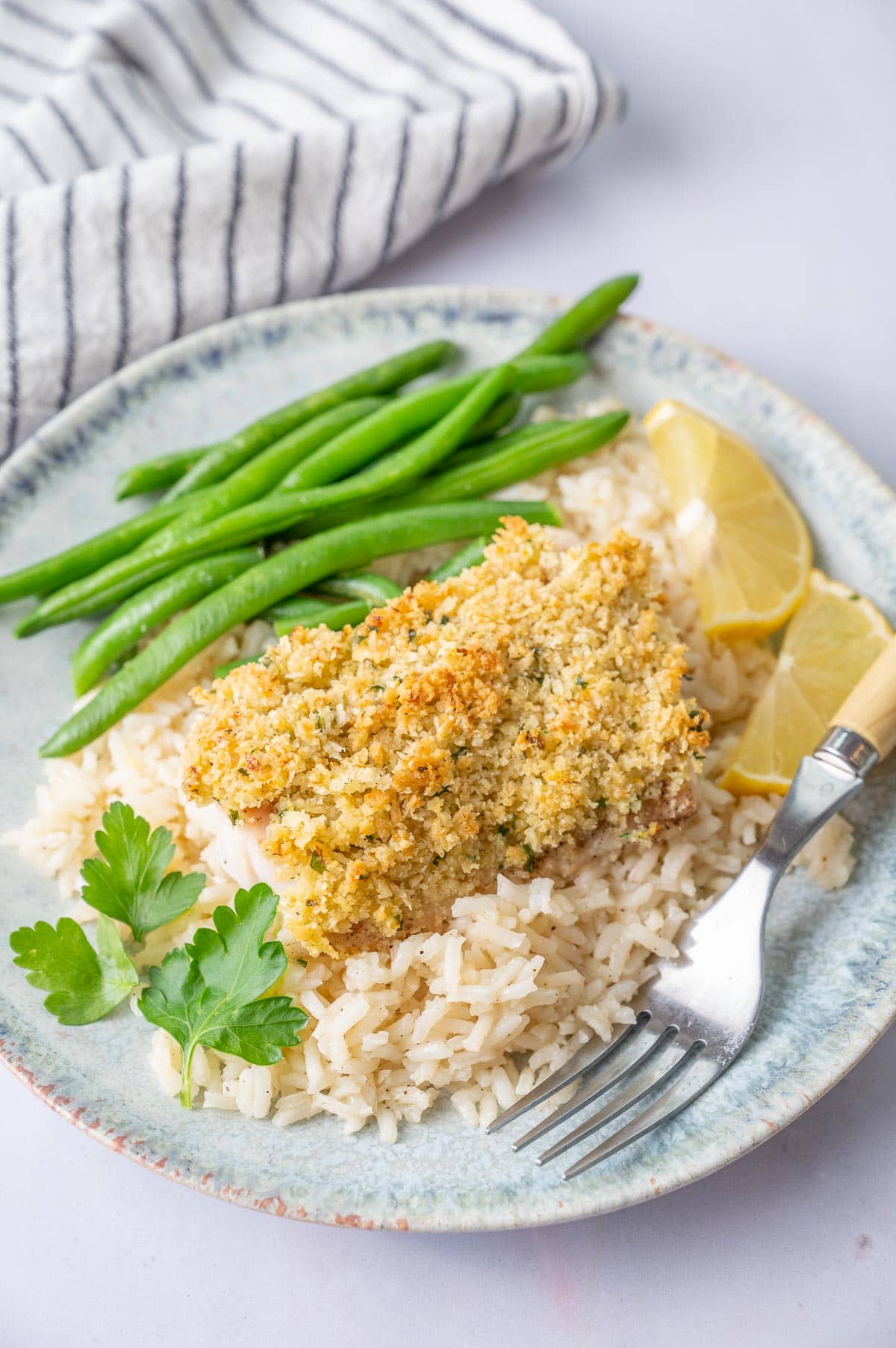 Parmesan crusted cod with butter garlic rice and green beans on a blue plate.