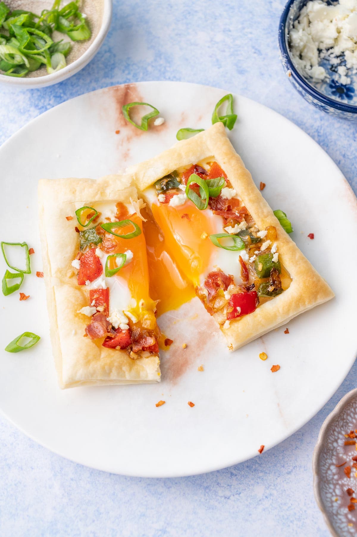 Puff pastry breakfast tart on a white plate cut in half with a runny egg yolk.