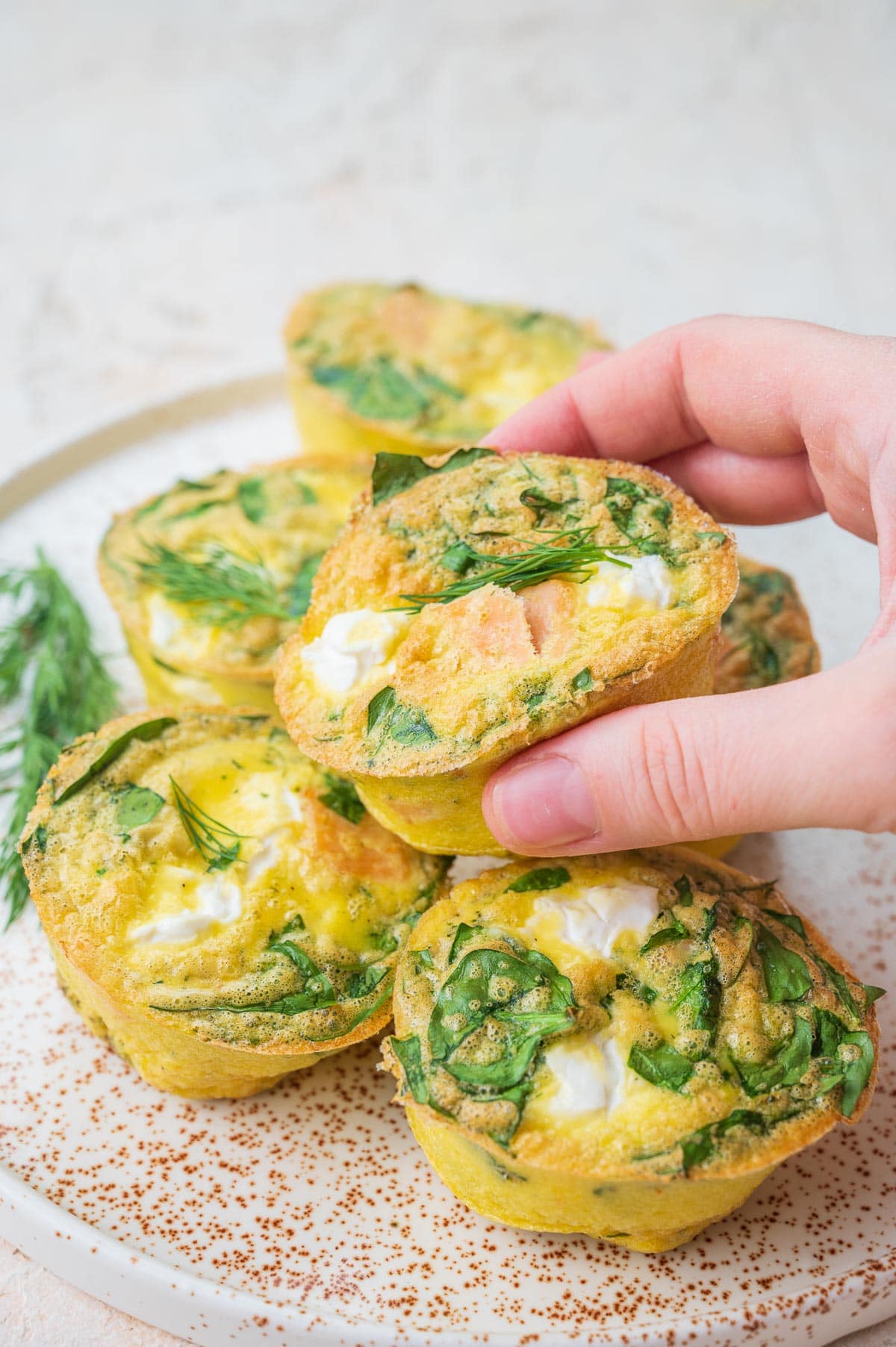 Smoked salmon egg muffins on a white plate. One muffin is being held in a hand.