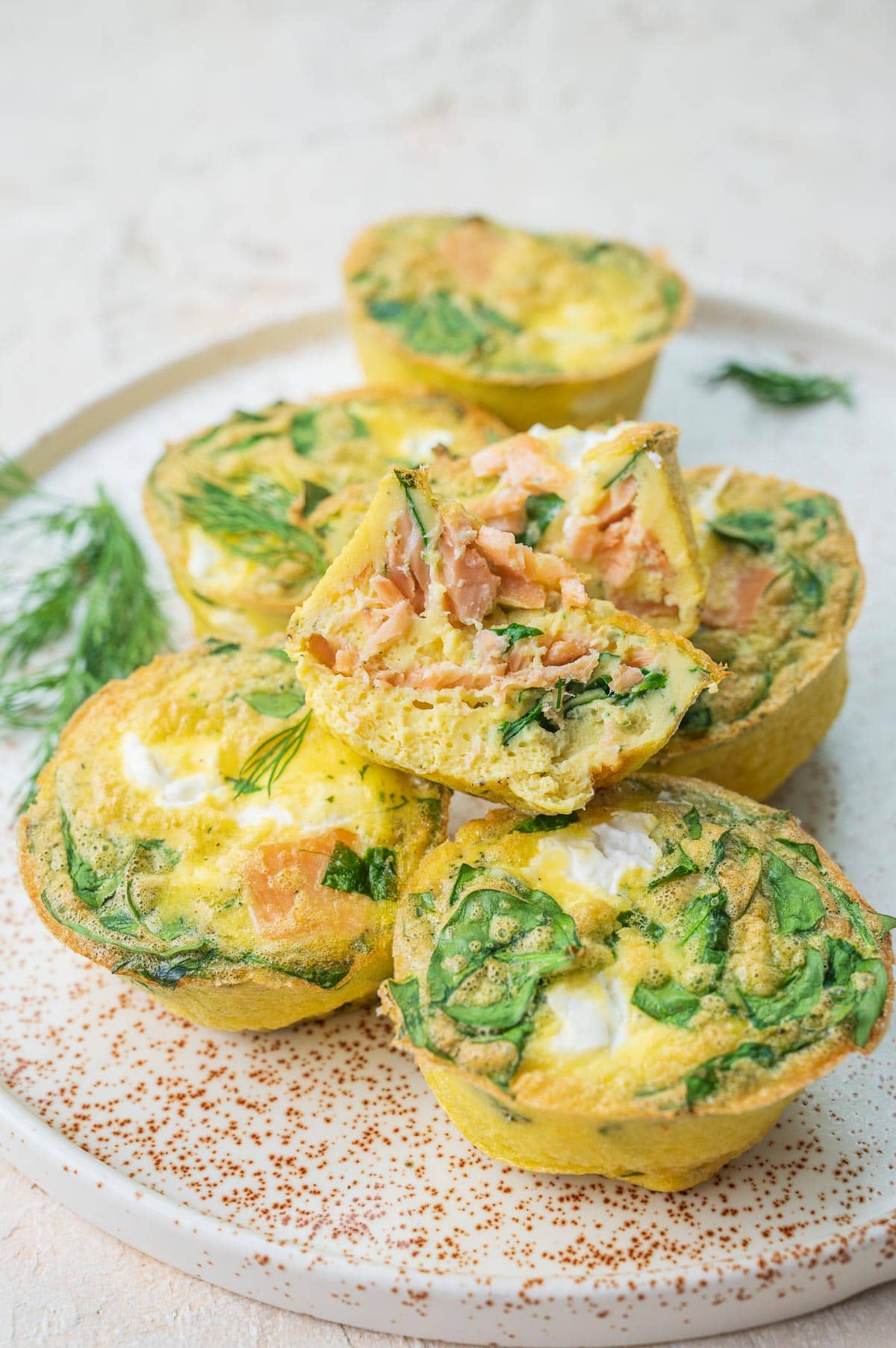 Smoked salmon egg muffins on a white plate. One muffin is cut in half.