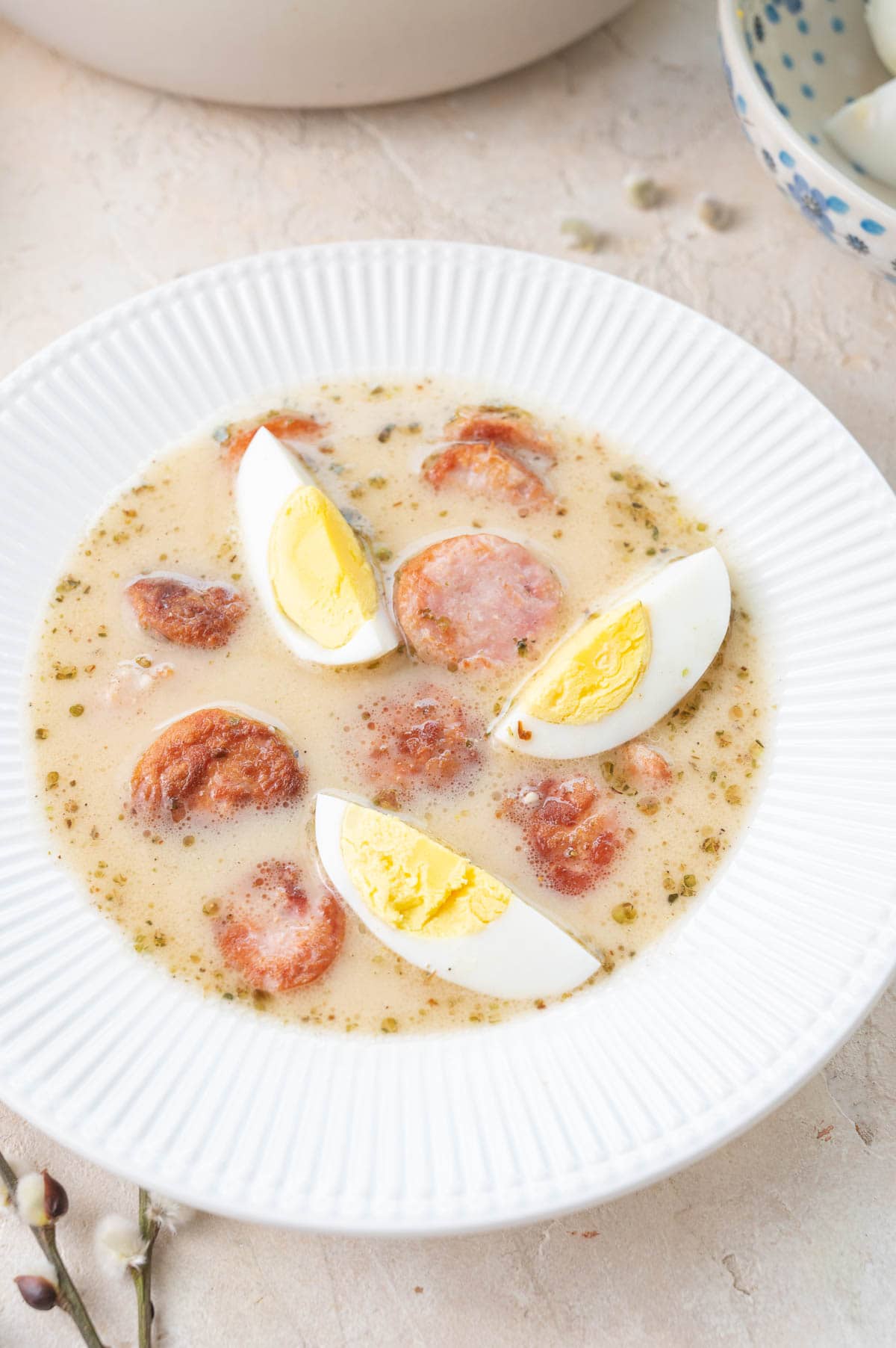 White borscht with sausage and eggs in a white bowl.