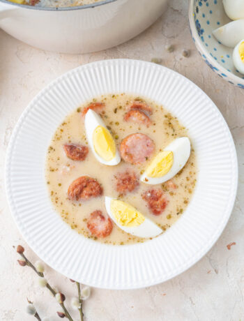 White borscht with sausage and eggs in a white bowl.