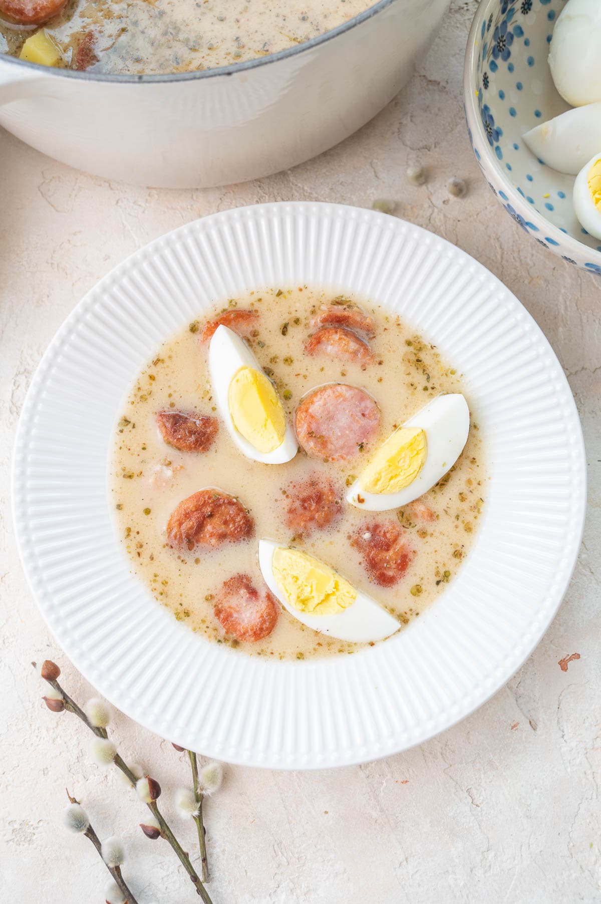 White borscht with sausage and eggs in a white bowl.