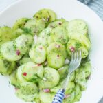 German cucumber salad in a white bowl with a fork on the side.