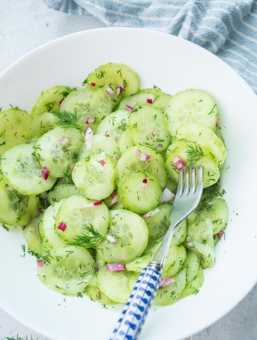 German cucumber salad in a white bowl with a fork on the side.