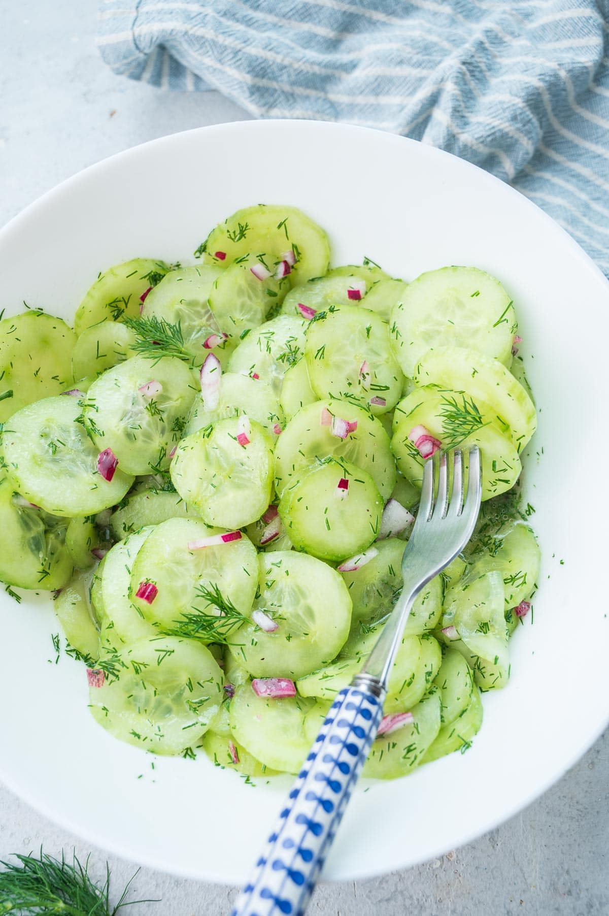 German cucumber salad in a white plate with a blue fork on the side.