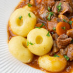 Kluski slaskie (Silesian dumplings) served with pork stew in a white plate.