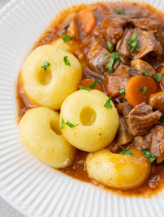 Kluski slaskie (Silesian dumplings) served with pork stew in a white plate.