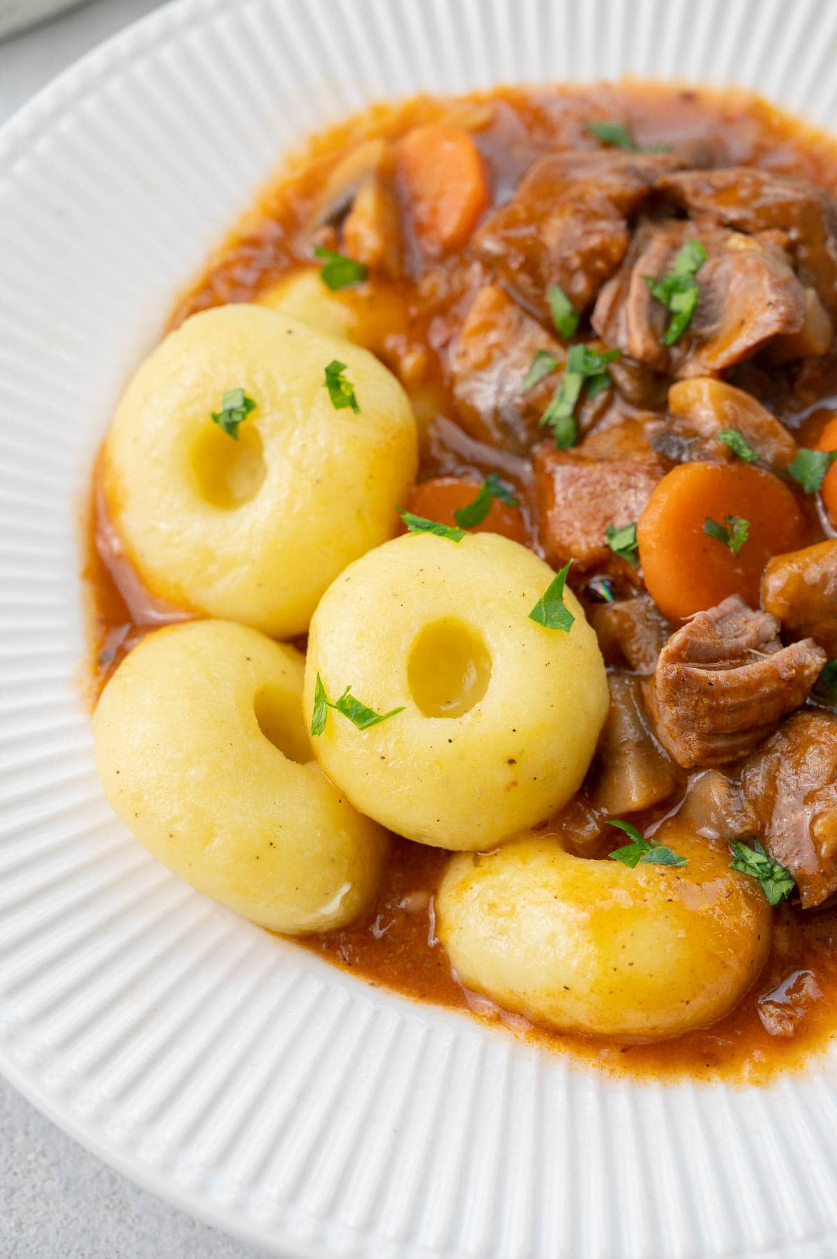 Kluski slaskie (Silesian dumplings) served with pork stew in a white plate.