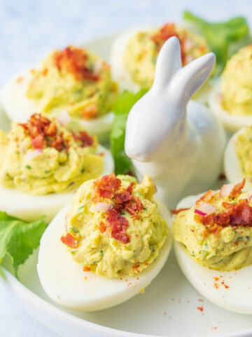 Avocado deviled eggs on a white plate with a bunny figure.