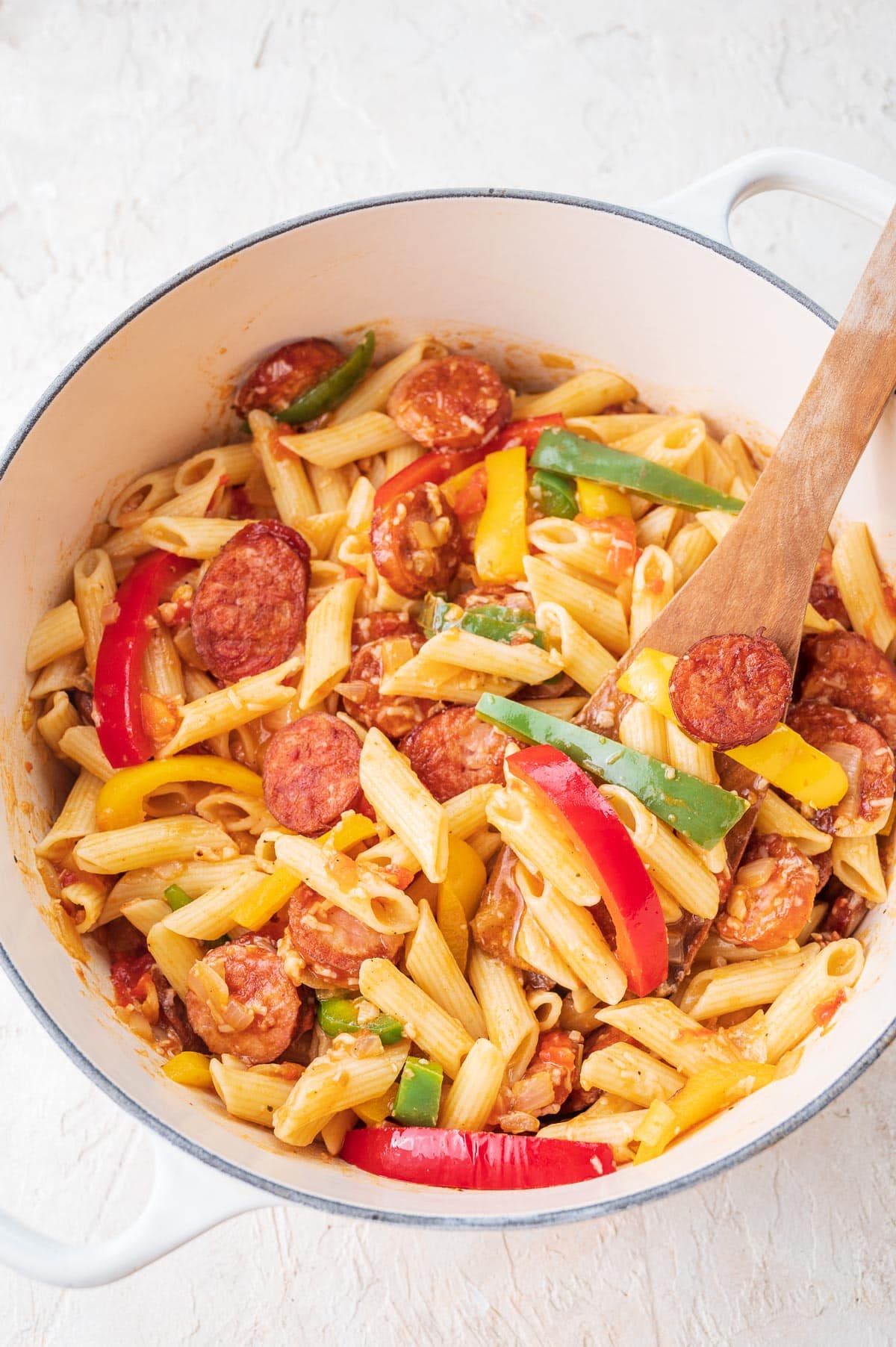 Pasta with sausage and bell peppers in a large white pot.