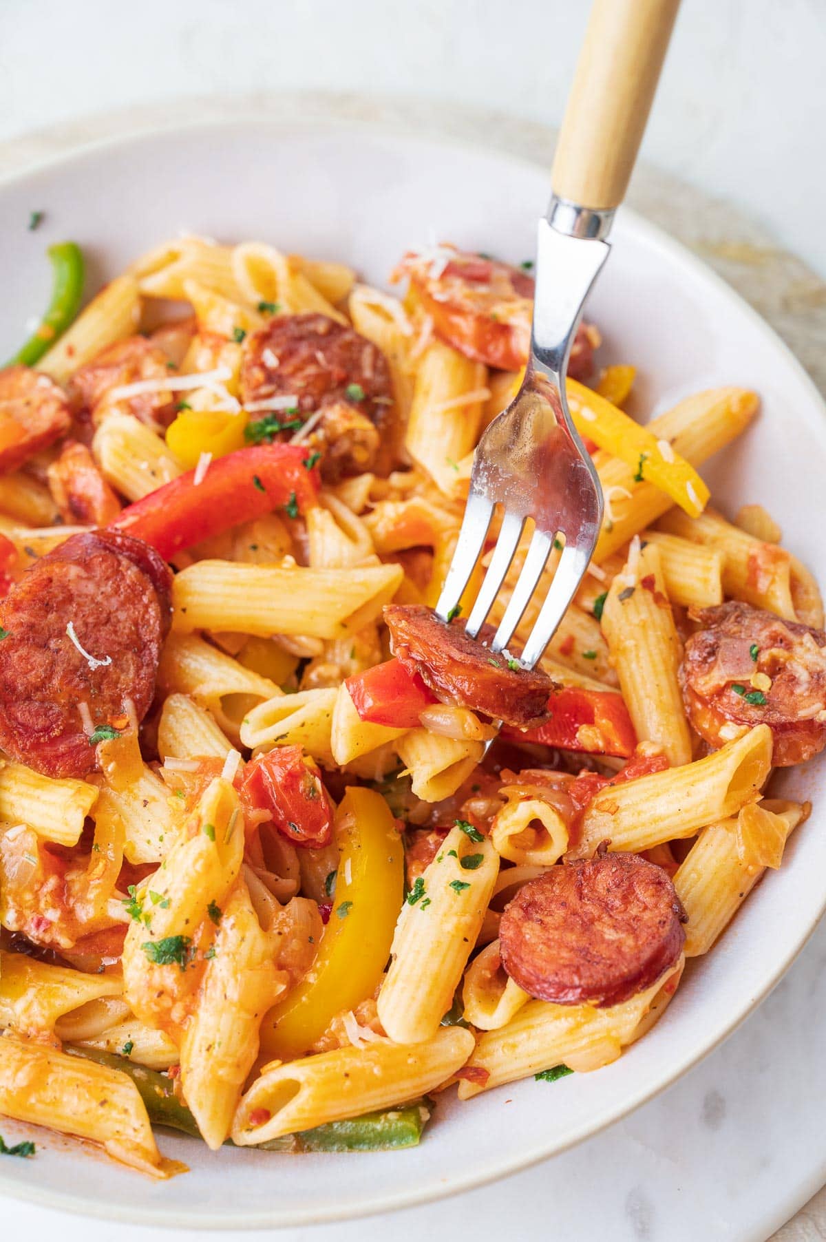 A close up photo of sausage pepper pasta in a white bowl.