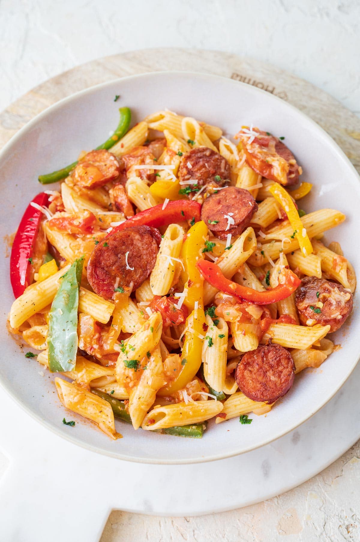 Pasta with sausage and bell peppers in a white bowl.