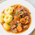 Polish pork stew served with dumplings in a white plate.