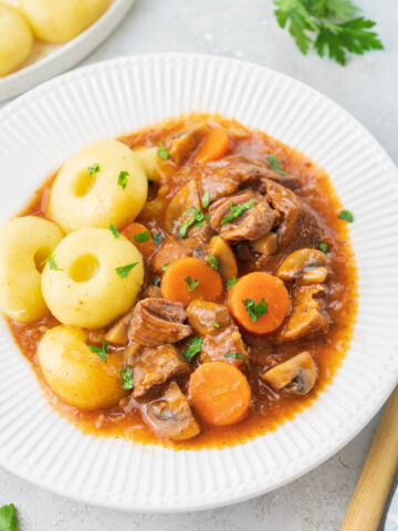 Polish pork stew served with dumplings in a white plate.