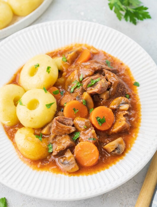Polish pork stew served with dumplings in a white plate.