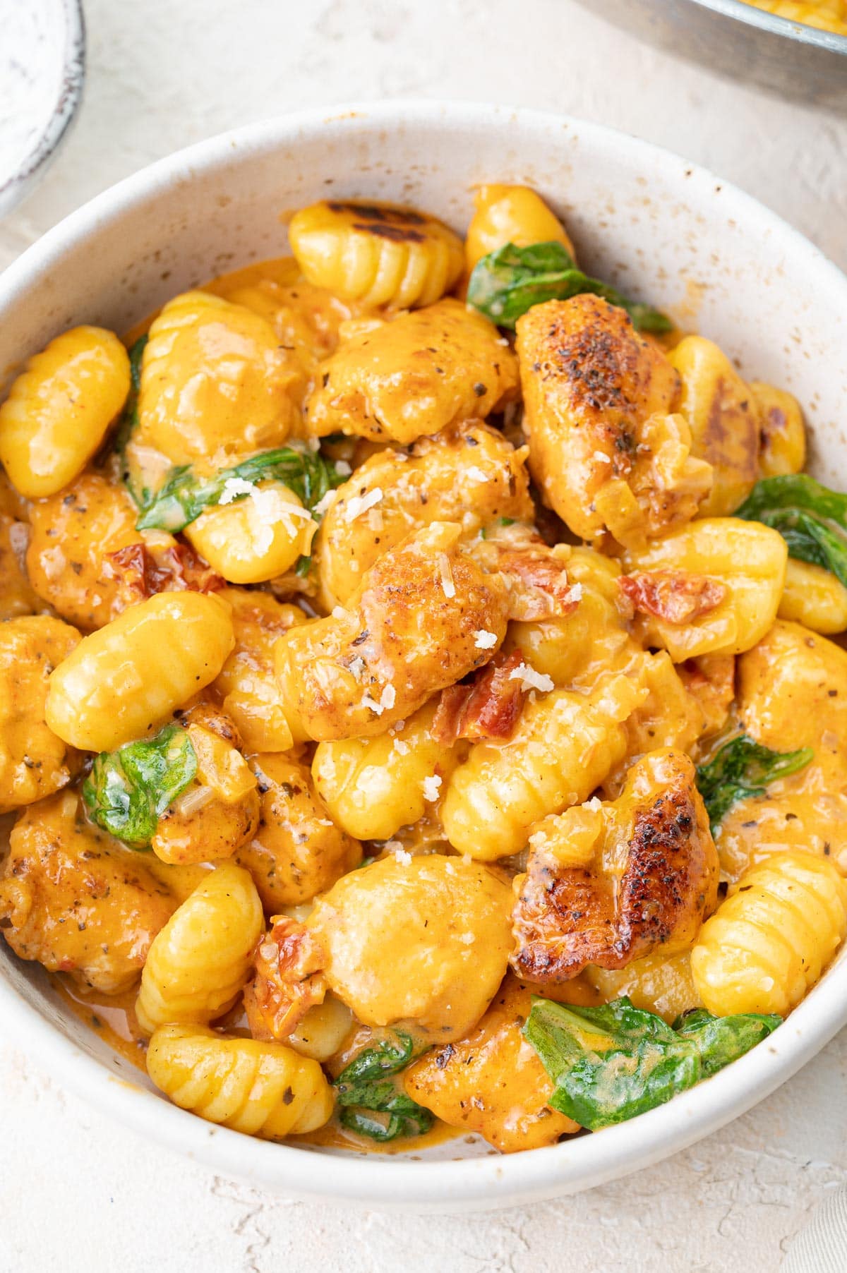 Creamy Tuscan chicken with gnocchi and spinach in a white bowl.