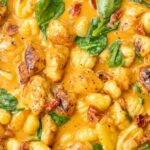 A close-up photo of creamy Tuscan chicken with gnocchi, sun-dried tomatoes, and spinach.