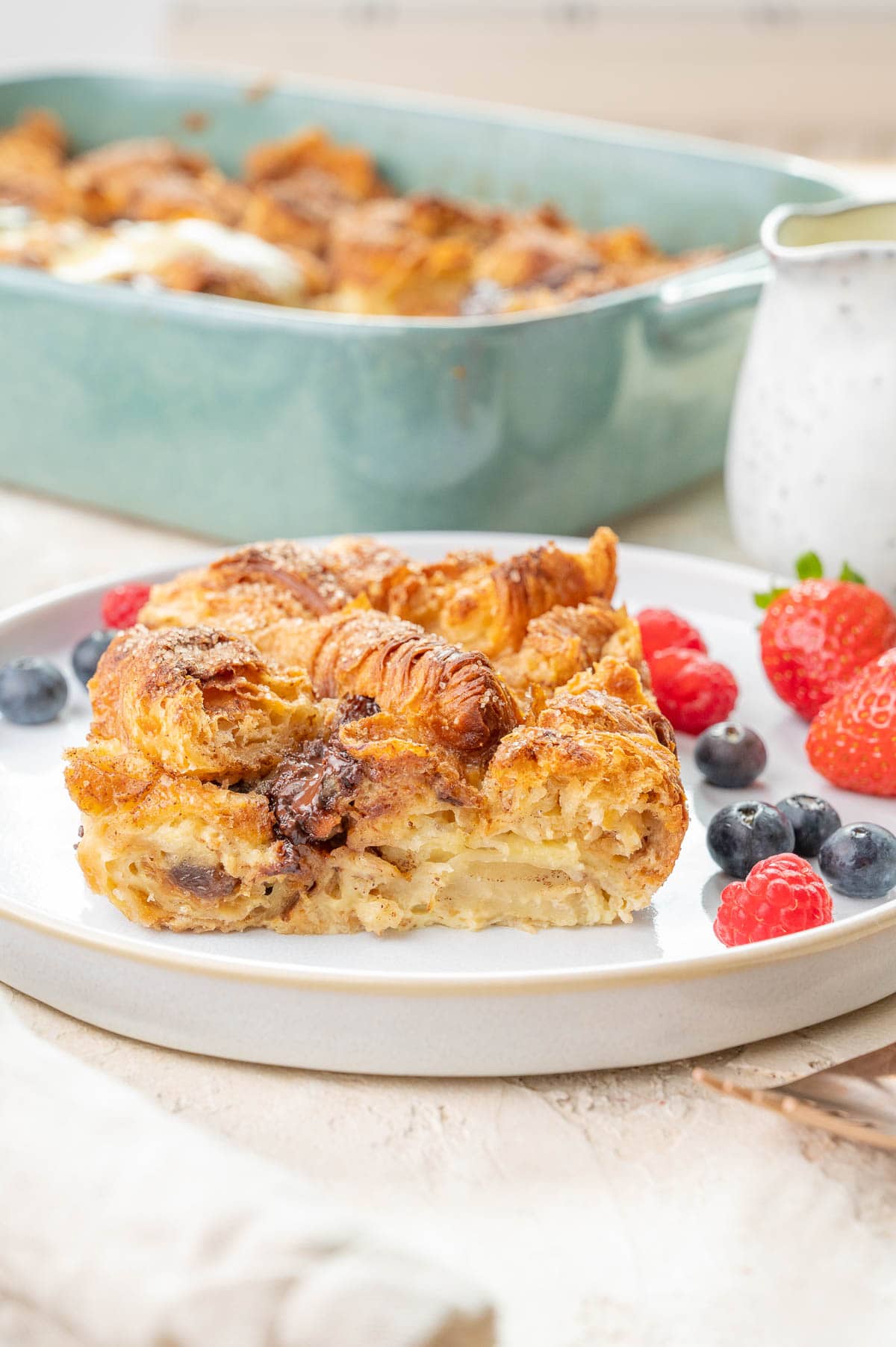 Croissant bread pudding served with berries on a white plate.