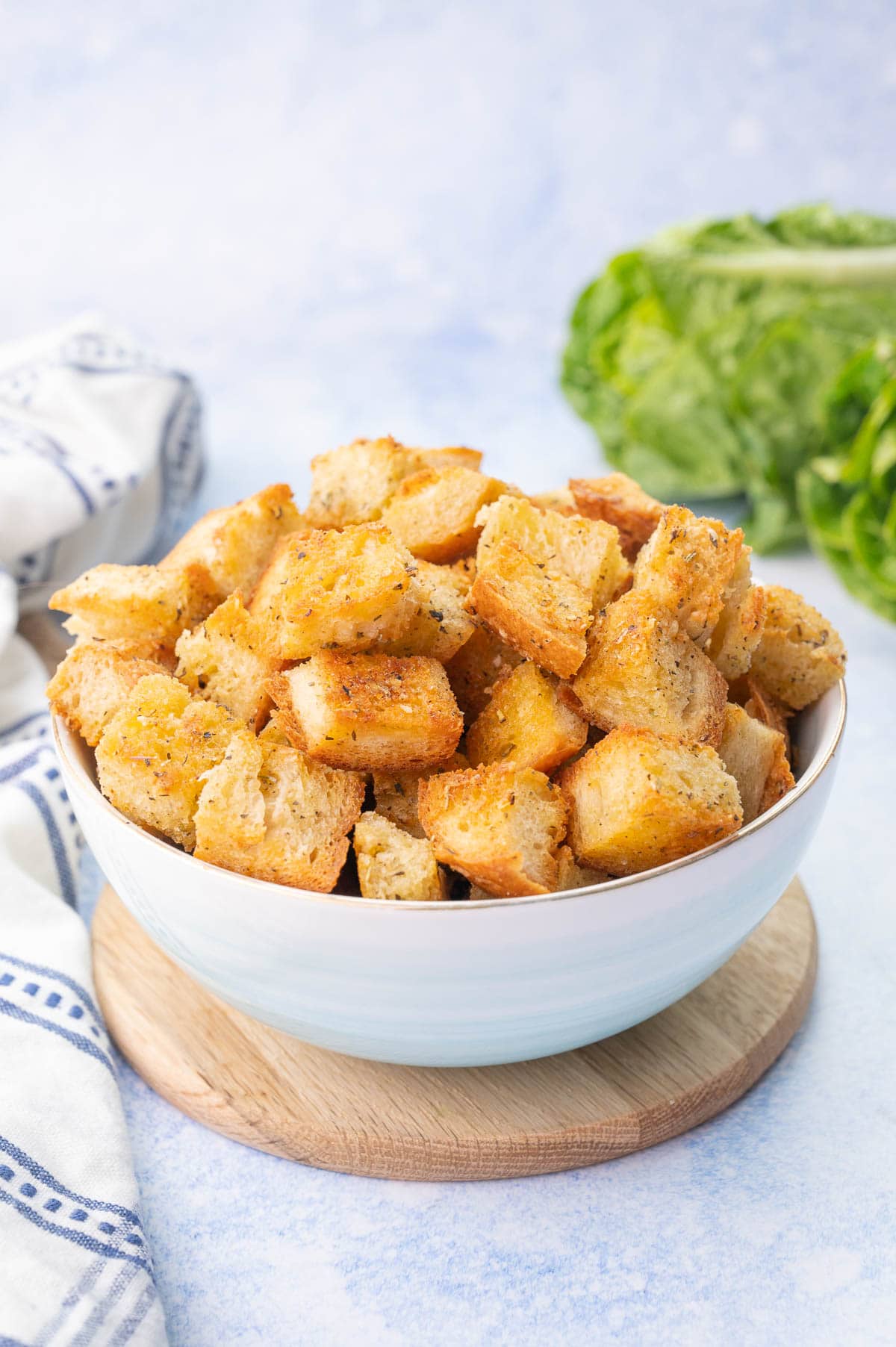 Homemade croutons in a blue bowl on a wooden board.