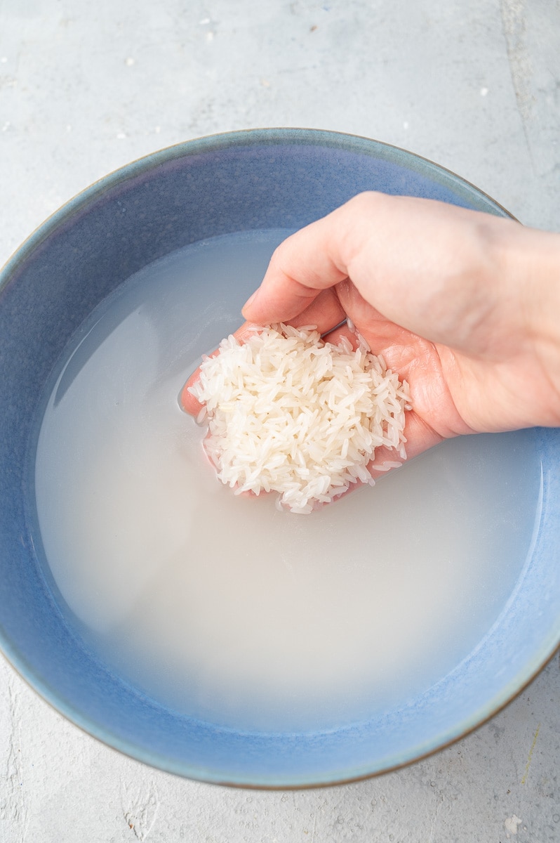 Jasmine rice is being rinsed in a blue bowl filled with water.