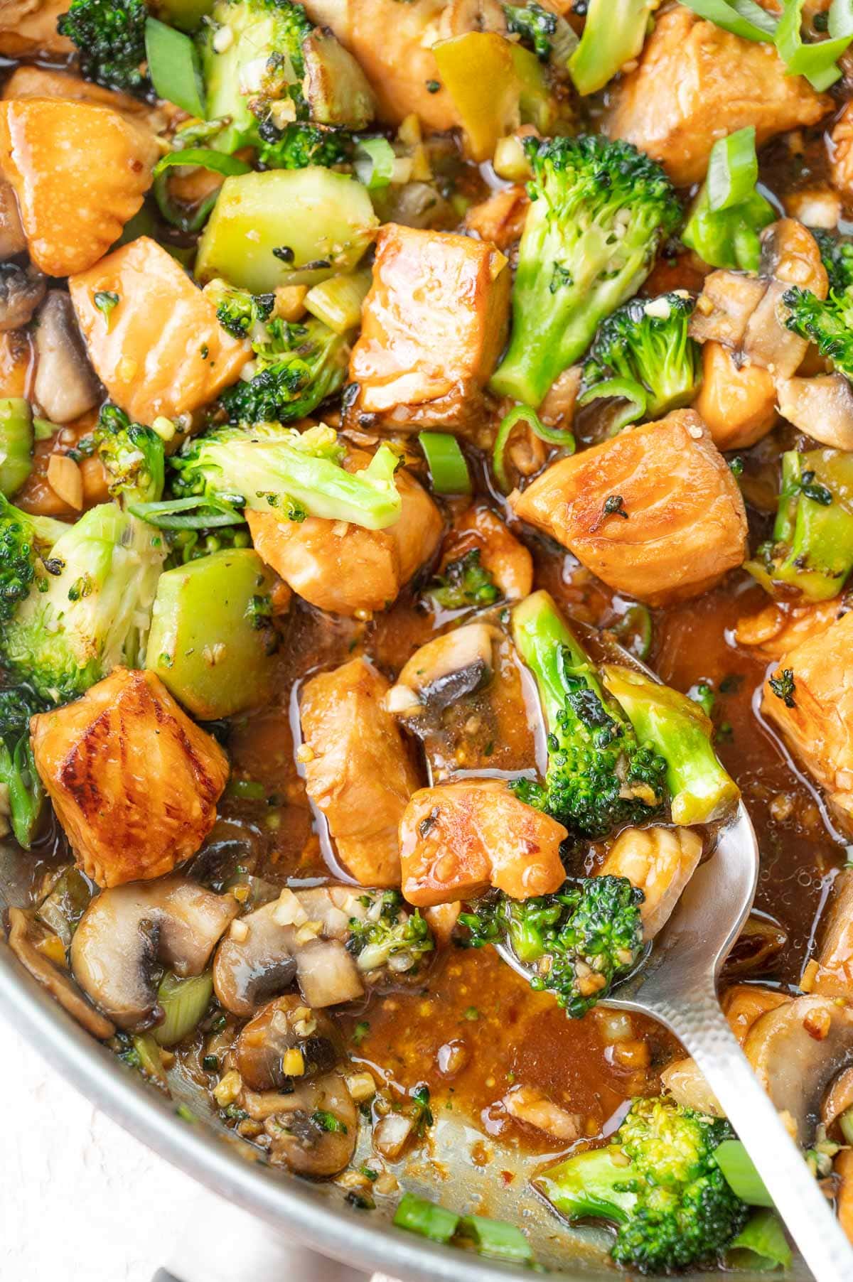 A close up photo of salmon stir fry with broccoli and mushrooms.