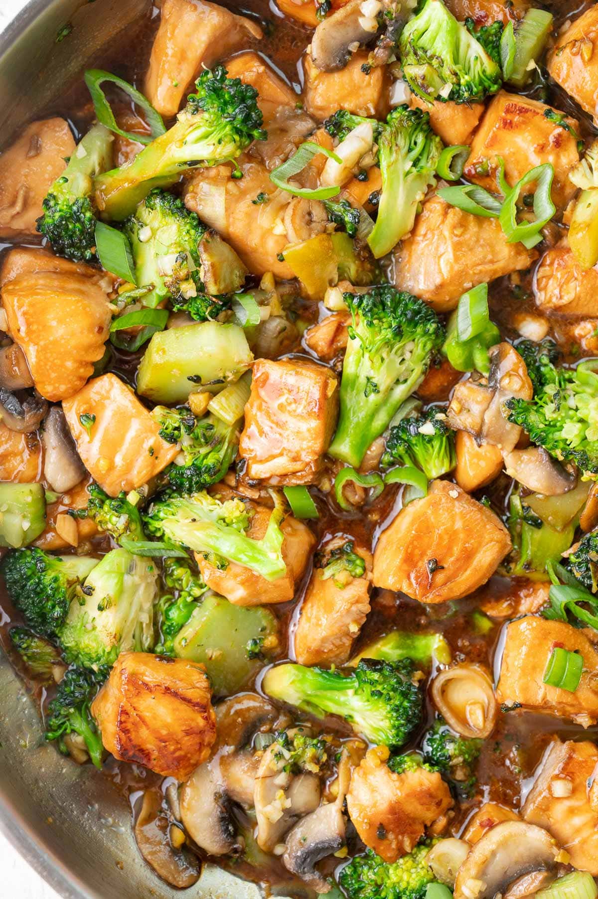 A close up photo of salmon stir fry with broccoli and mushrooms.