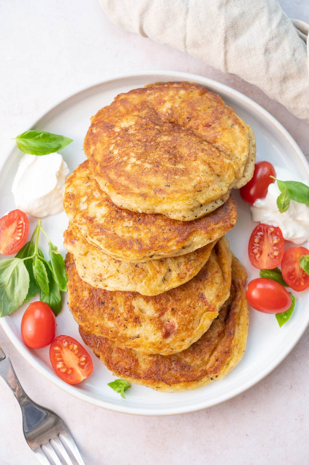 Savory Pancakes on a white plate served with cherry tomatoes, basil, and yogurt.