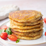 A stack of savory pancakes on a white plate served with tomatoes and basil.
