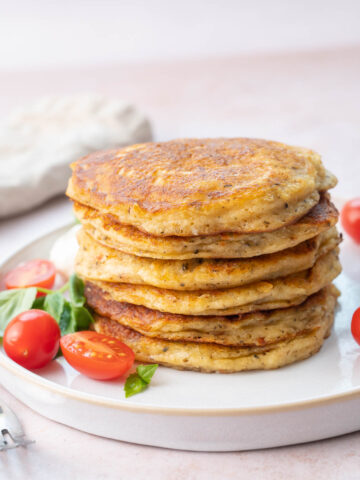 A stack of savory pancakes on a white plate served with tomatoes and basil.