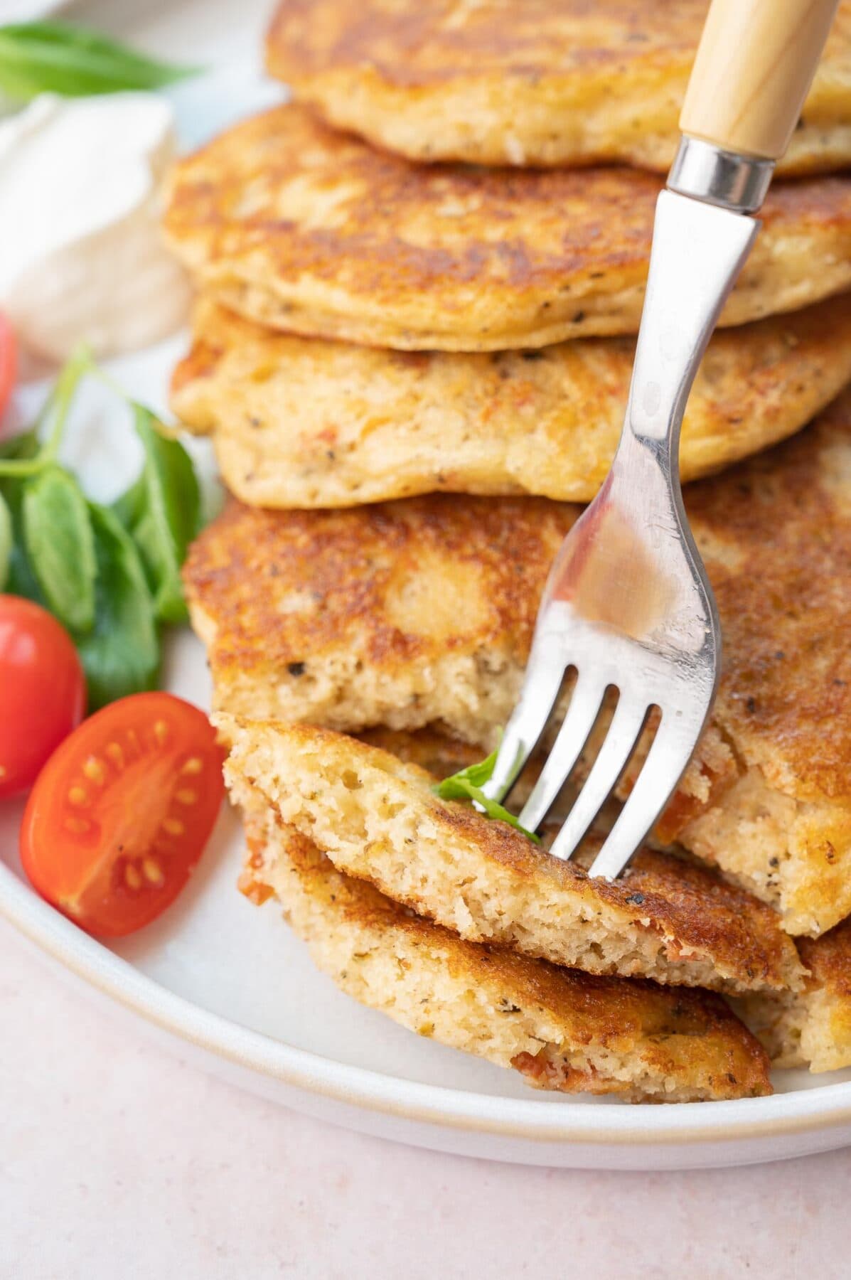 Two pieces of savory pancakes stuck on a fork on a white plate.