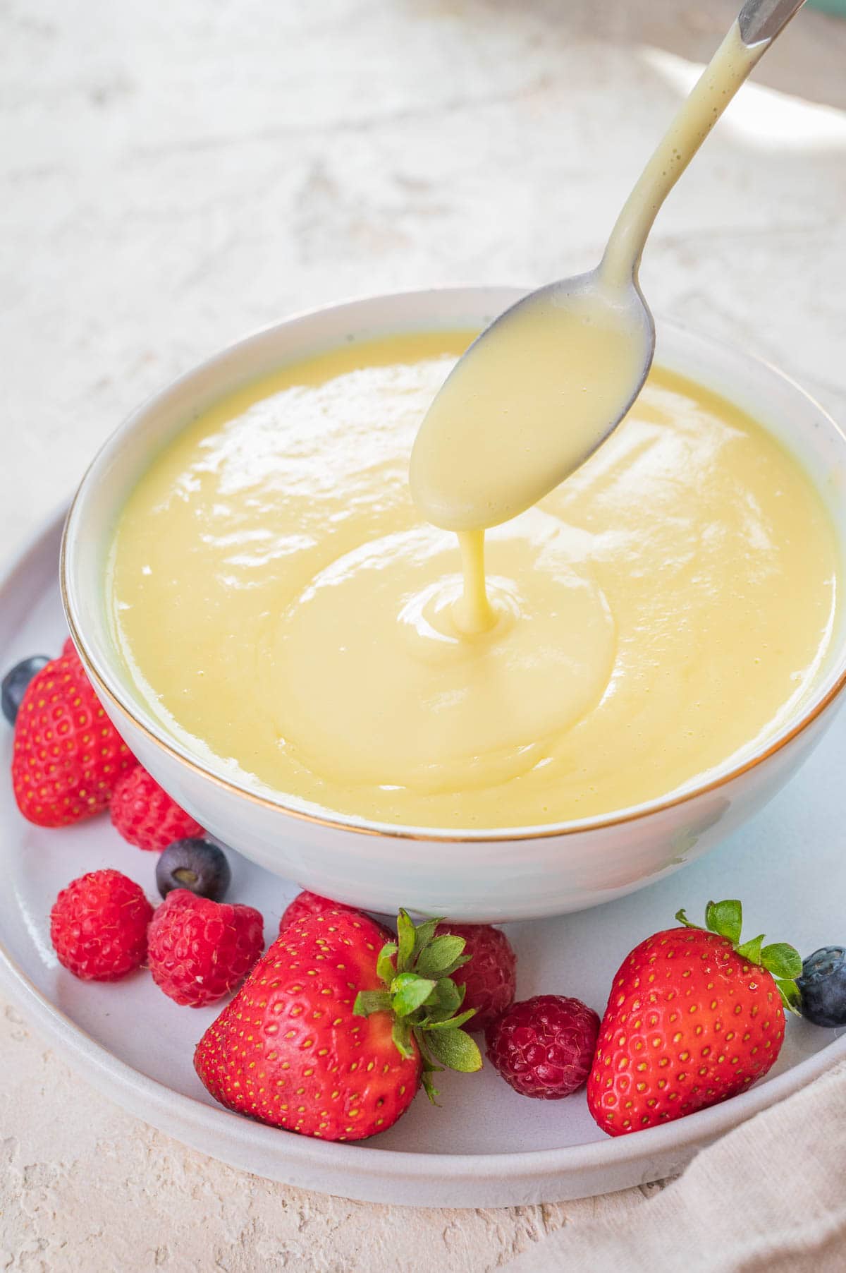 Vanilla sauce in a white bowl served with fresh berries.