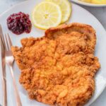 Wiener Schnitzel on a beige plate with lemon slices and red currant jam.
