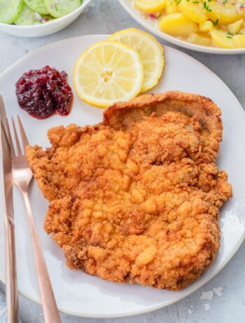 Wiener Schnitzel on a beige plate with lemon slices and red currant jam.