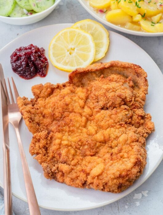 Wiener Schnitzel on a beige plate with lemon slices and red currant jam.