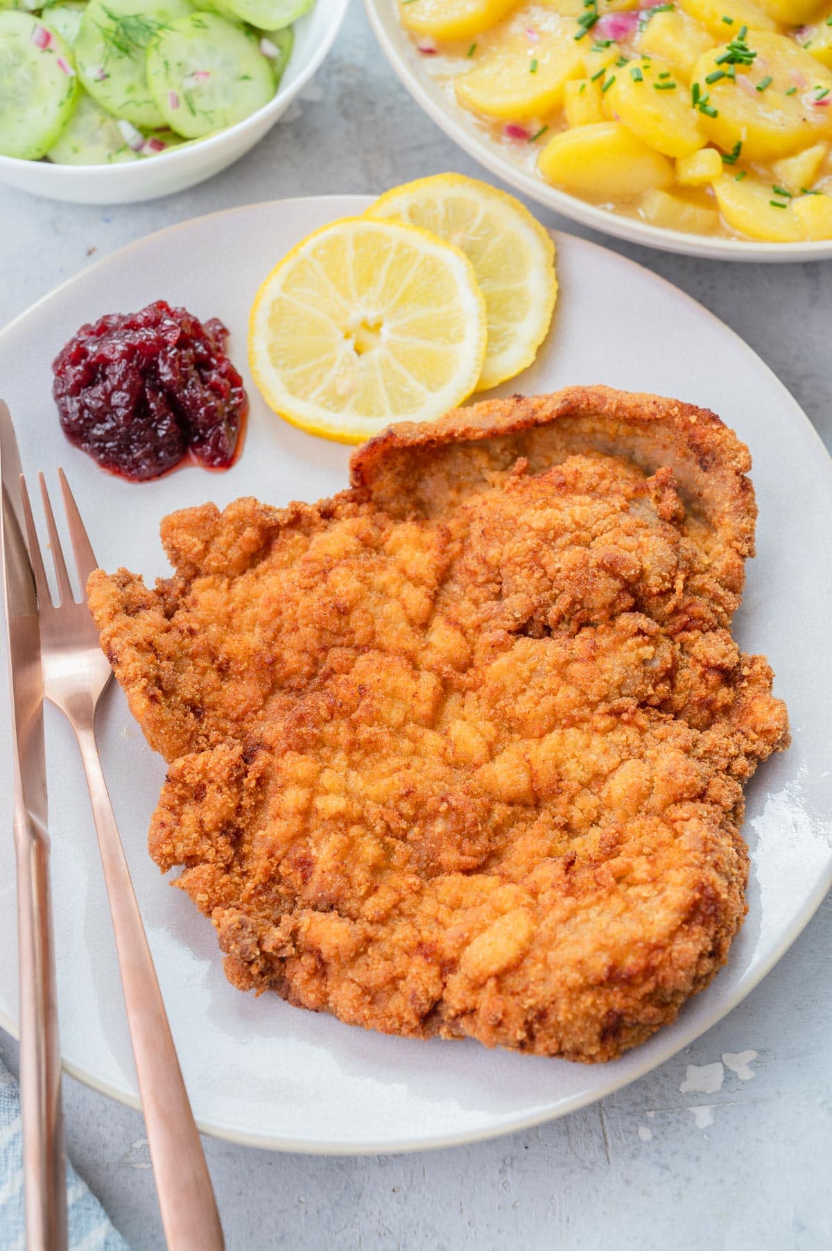 Wiener Schnitzel on a beige plate with lemon slices and red currant jam.