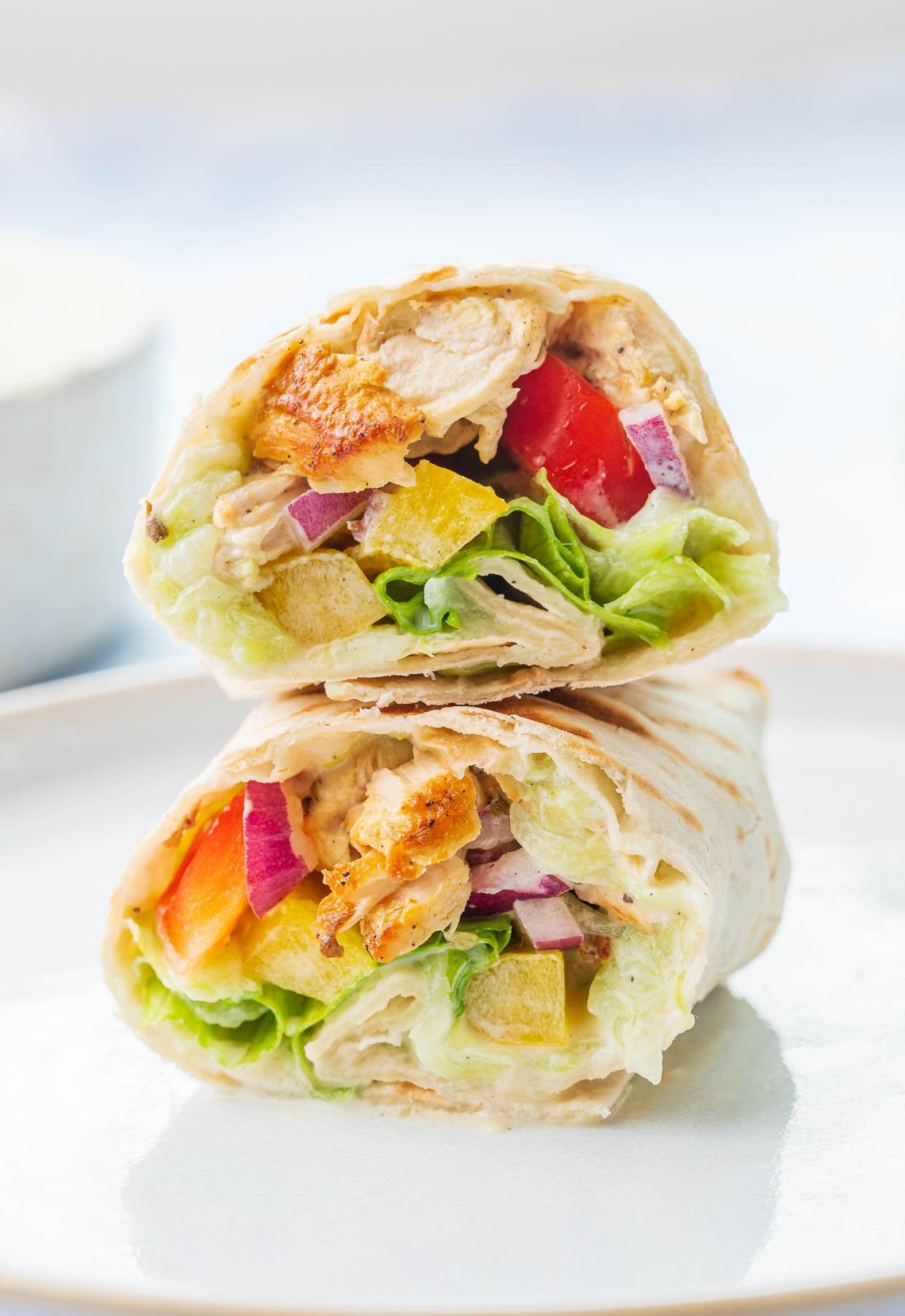 A stack of 2 cut in half Greek chicken wraps on a white plate.
