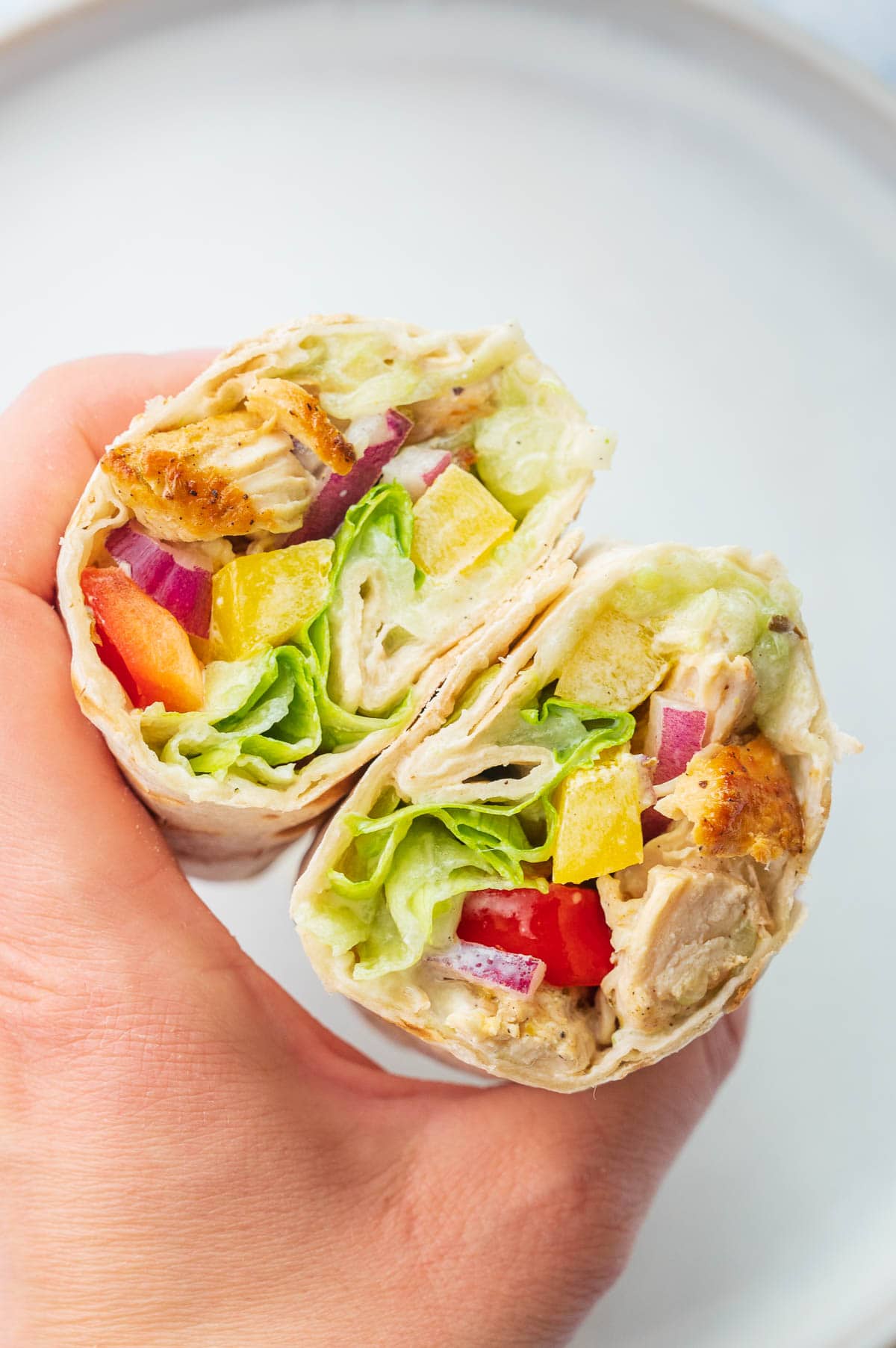 Two cut in half Greek chicken wraps are being held in a hand.