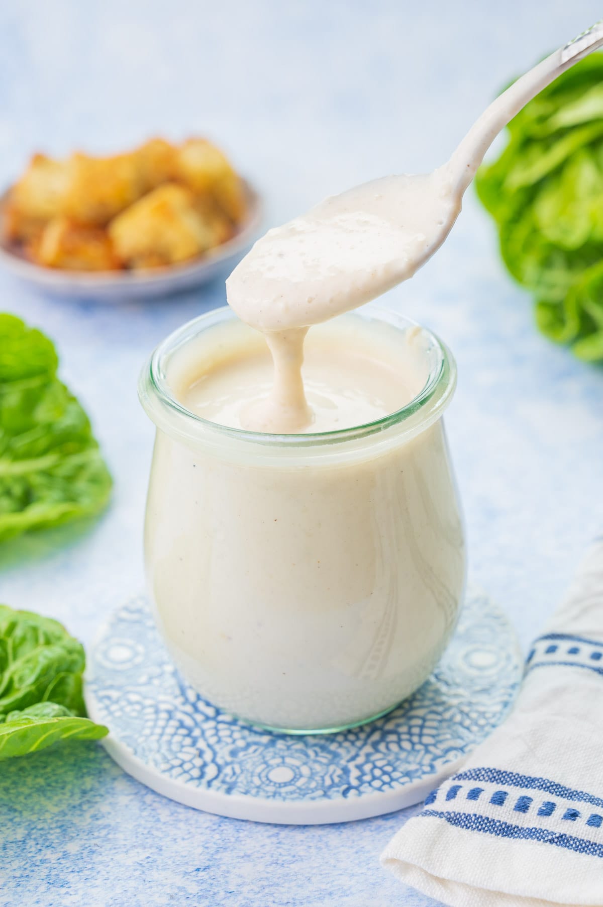 Caesar Salad Dressing in a small jar and it's flowing off a spoon.