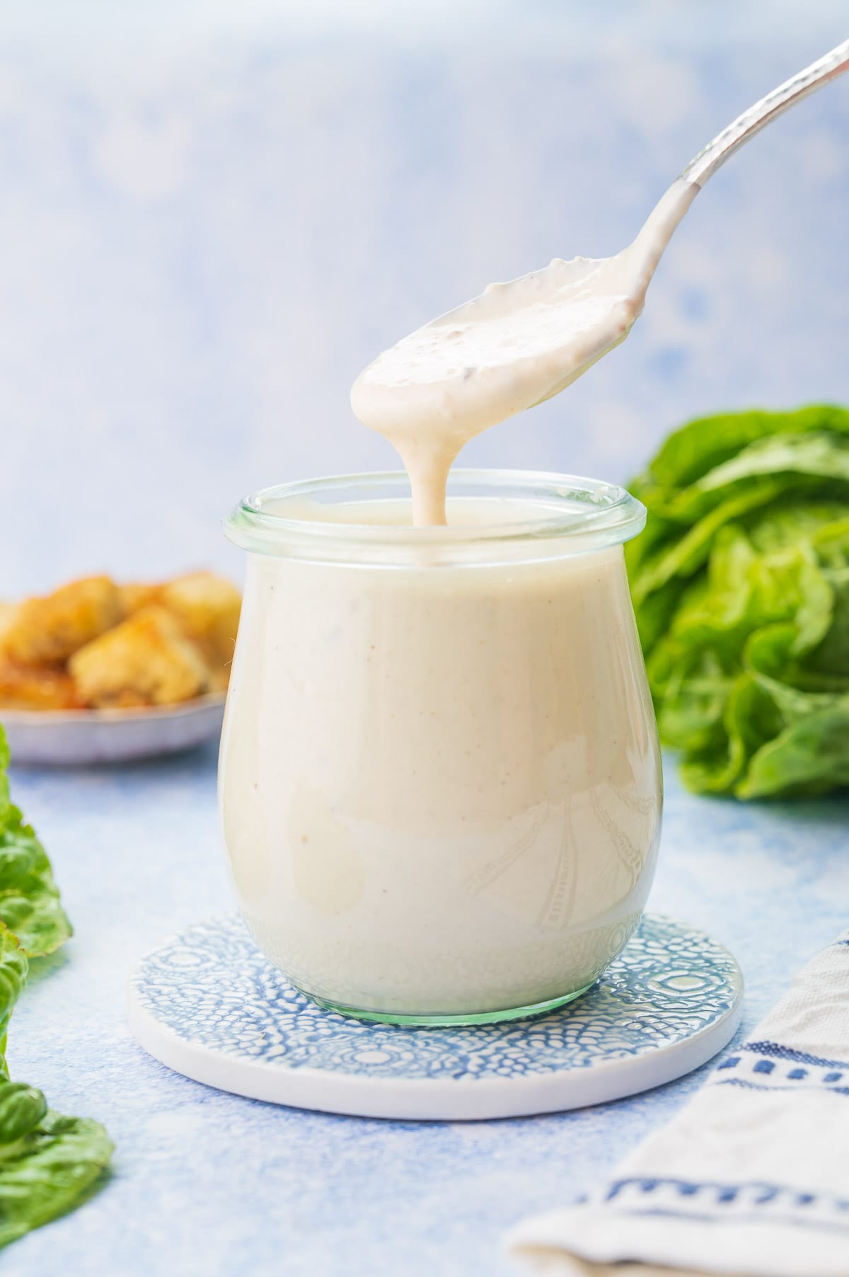 Caesar Salad Dressing in a small jar and it's flowing off a spoon.