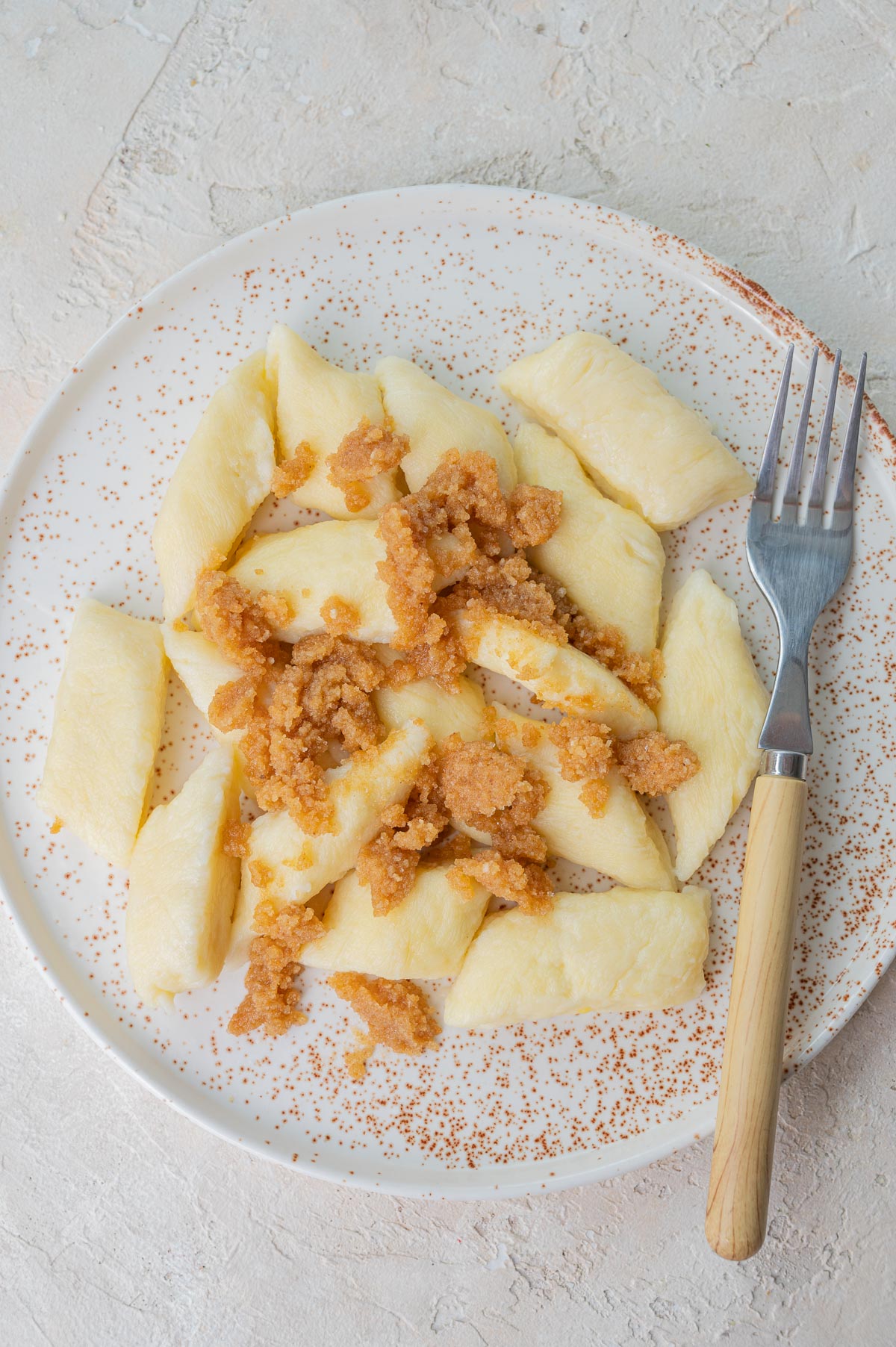 Potato and cheese leniwe on a white plate topped with buttered breadcrumbs.