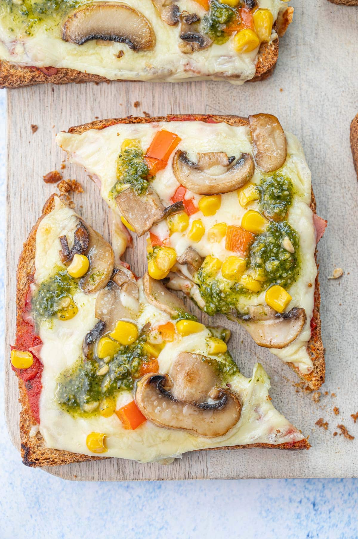 Pizza toast on a chopping board cut in half.