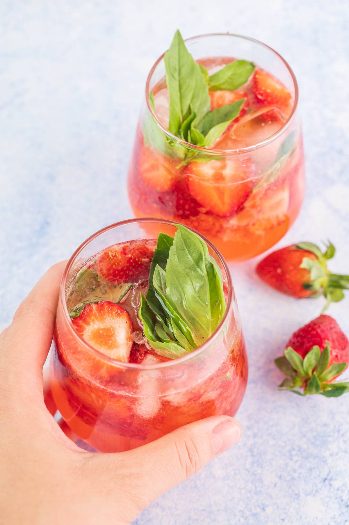 Strawberry basil cocktail in a glass held in a hand.